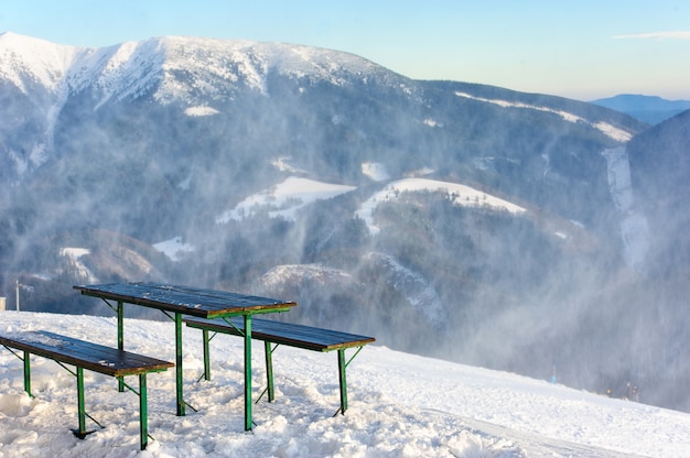 Bänke und der Tisch auf einem Berggipfel mit einem schönen Blick über eine Winterszene mit Bergen, Bäumen und Schnee