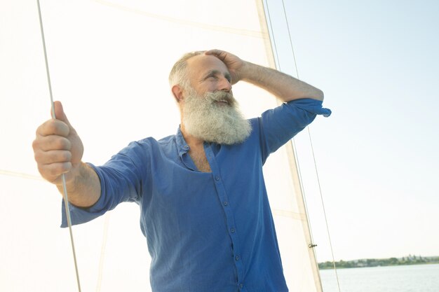 Bärtiger älterer Mann auf Segelboot oder Yacht, die auf See schwimmt.