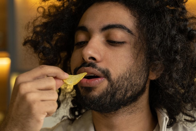 Bärtiger arabischer Mann mit verworrenen Haaren isst gerne Chips