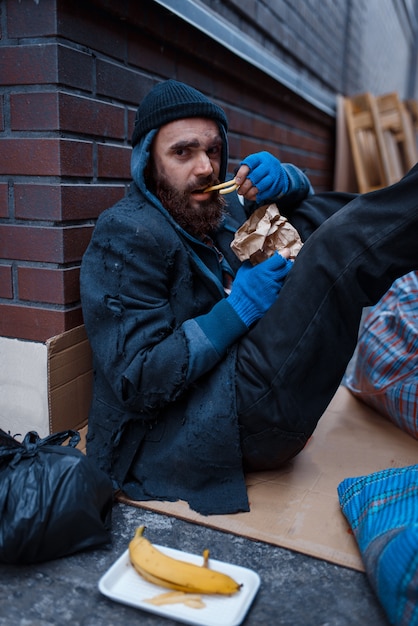 Foto bärtiger bettler isst burger auf stadtstraße