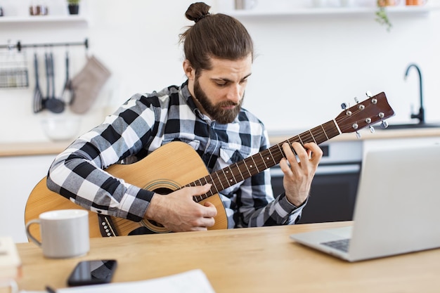 Bärtiger Erwachsener posiert mit Gitarre, während er zu Hause einen angenehmen Zeitvertreib genießt