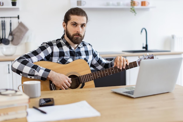 Bärtiger Erwachsener posiert mit Gitarre, während er zu Hause einen angenehmen Zeitvertreib genießt