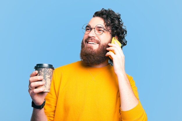 Bärtiger glücklicher Hipster-Mann, der Tasse Kaffee hält und am Telefon spricht
