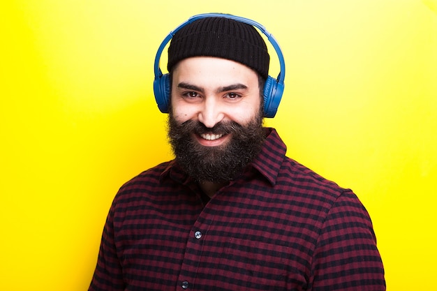 Bärtiger Hipster-Mann, der einen schwarzen Hut trägt und über drahtlose Kopfhörer Musik hört