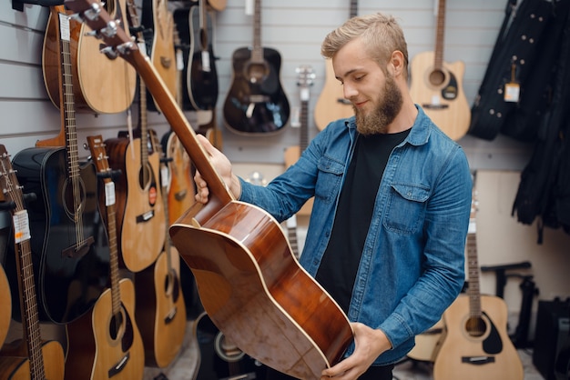 Bärtiger junger Mann, der akustische Gitarre im Musikgeschäft wählt.