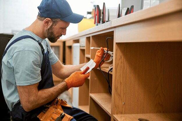 Bärtiger junger Mann, der elektrische Drähte des Schreibtisches repariert