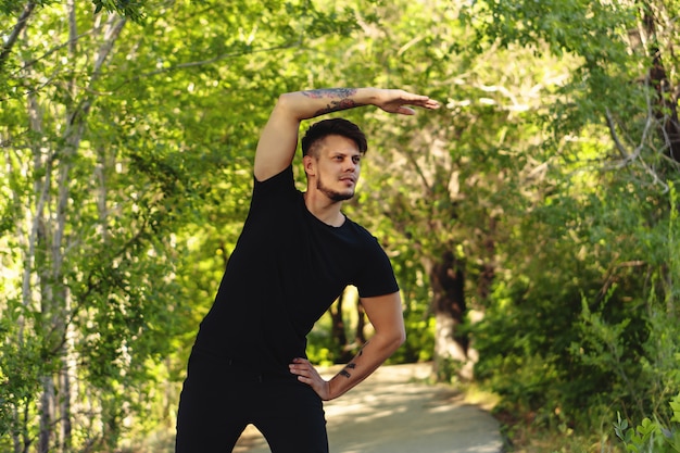 Bärtiger junger Mann, der im Park vor dem Joggen trainiert. Speicherplatz kopieren