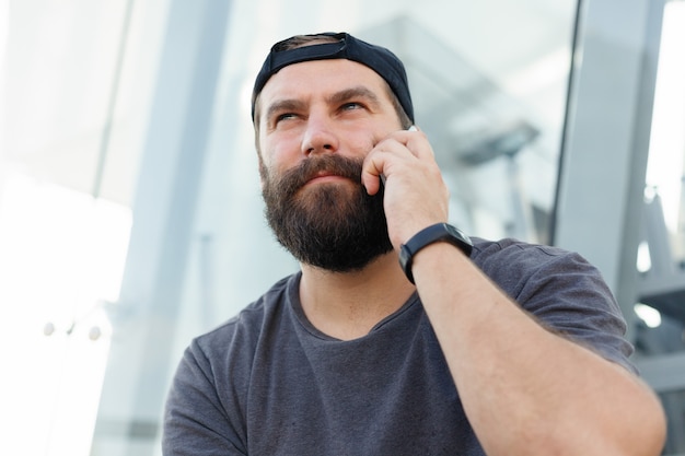 Bärtiger Kerl, der am Telefon spricht. Hipster junger Mann am Telefon in einem städtischen Hintergrund