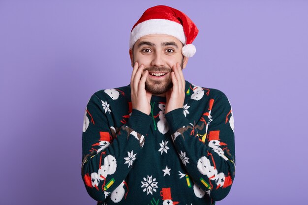 Bärtiger Kerl kleidet Weihnachtsmütze und Fanny-Pullover mit Schneemann auf lila