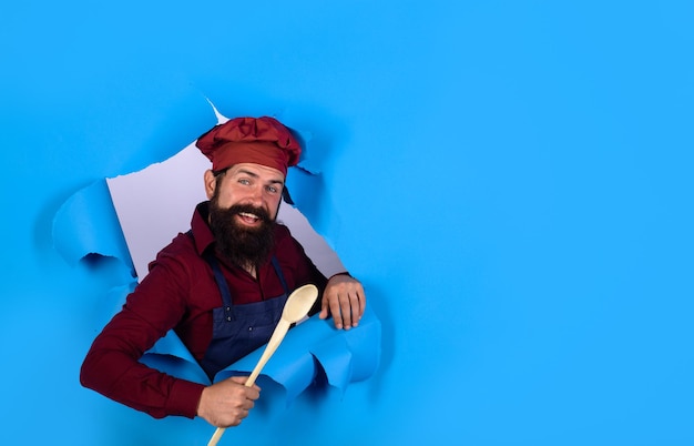 Bärtiger Koch mit Holzlöffel, der durch den bärtigen Küchenchef aus Papier schaut, der sich darauf vorbereitet, Essen zu kochen?