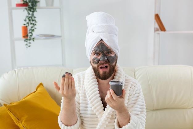 Bärtiger lustiger Mann, der sich mit einer kosmetischen Maske auf seinem Gesicht aus schwarzem Ton amüsiert