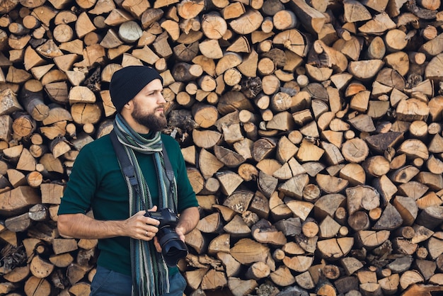 Bärtiger männlicher Fotograf mit Digitalkamera im Freien in der Nähe einer Brennholzwand