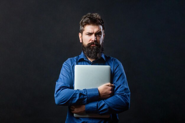 Bärtiger männlicher Geschäftsmann, der einen Computer in seinen Händen hält, die auf schwarzem Hintergrund lokalisiert werden Geschäftsmann, der seinen Laptop-PC verwendet Holding-Laptop-Computer Ernsthaft gutaussehender bärtiger Mann Arbeiter Laptop