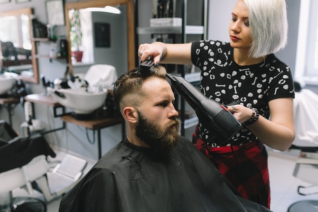 Bärtiger Mann am Friseur mit Haartrockner beim Sitzen im Stuhl am Friseursalon.