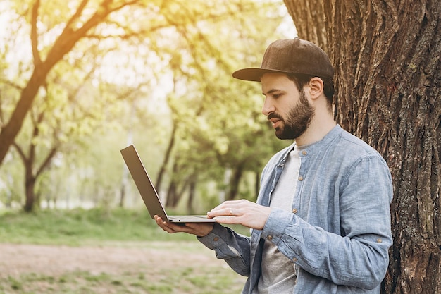 Bärtiger Mann, der an sonnigen Tagen mit Computer im Park arbeitet Naturreise und Entspannung im Freien