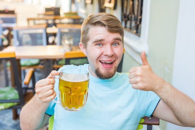 Bärtiger Mann, der Bier aus einem Bierkrug trinkt. Zeigt das Zeichen Daumen hoch.