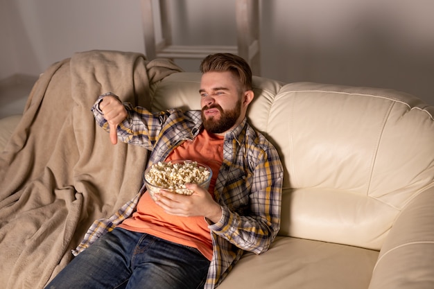 Bärtiger Mann, der Film- oder Sportspielfernsehen sieht, das Popcorn im Haus bei Nachtkino-Meisterschaft isst und