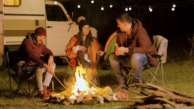 Bärtiger Mann, der seinen Freunden am Lagerfeuer einen lustigen Witz erzählt. Retro-Wohnmobil. Camping Zelt.