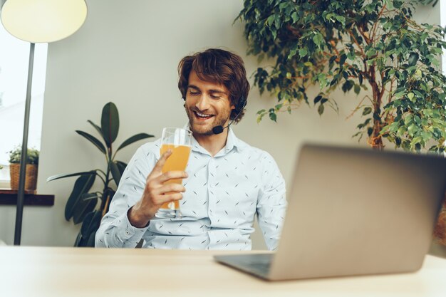 Bärtiger Mann, der seinen Laptop benutzt, während er ein Glas Bier trinkt