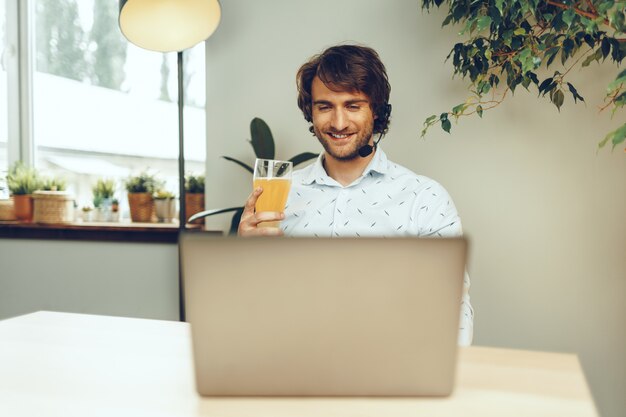 Bärtiger Mann, der seinen Laptop benutzt, während er ein Glas Bier trinkt