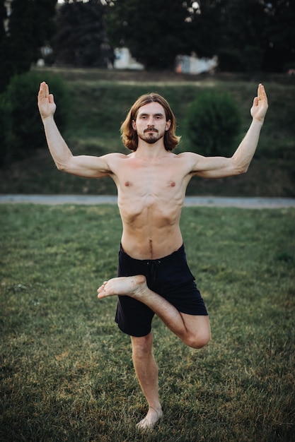 Bärtiger Mann, der Yoga im grünen Park tut