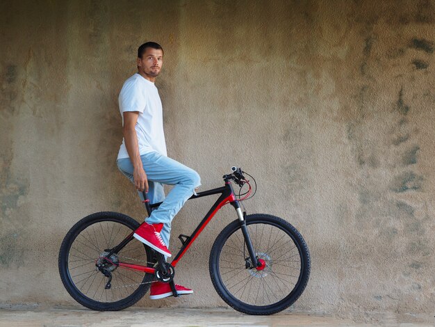 Bärtiger Mann, gekleidet in Jeans und einem roten Turnschuh auf einem Fahrrad