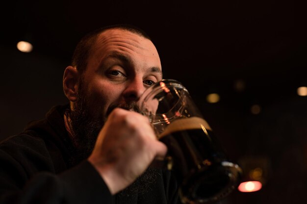 Foto bärtiger mann hält ein glas bier, während er in einer kneipe sitzt bierzeit alkoholgetränke