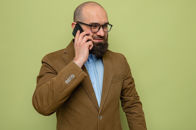 Bärtiger Mann im braunen Anzug mit Brille, der fröhlich lächelt, während er auf dem Handy auf grünem Hintergrund spricht