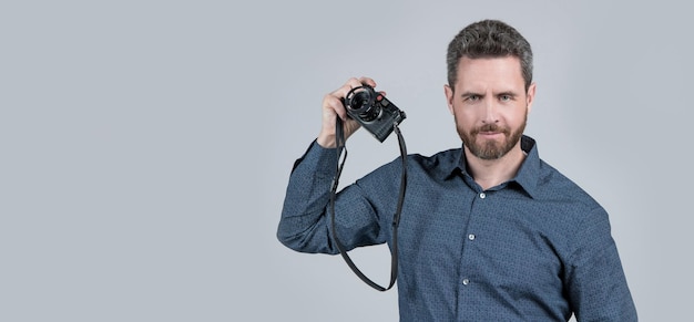 Bärtiger Mann im Freizeithemd hält Filmkamera grauer Hintergrund analoge Fotografie