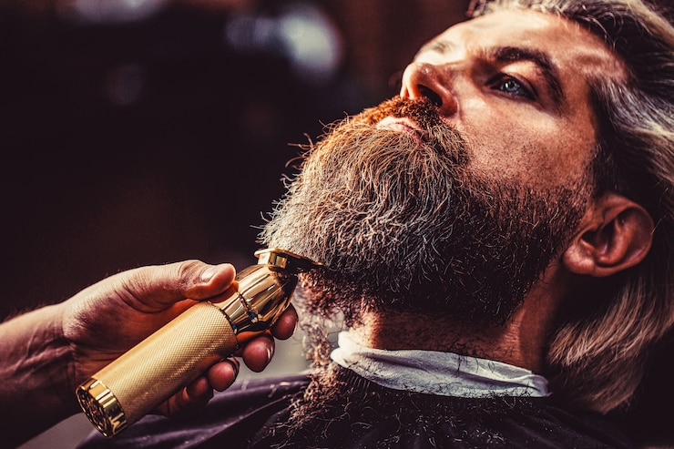 Foto bärtiger mann im friseursalon. mann, der friseur im friseursalon besucht. barber arbeitet mit einem bartschneider. hipster-kunde bekommt haarschnitt.
