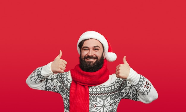 bärtiger Mann in der Weihnachtsmütze, der Daumen hoch zeigt