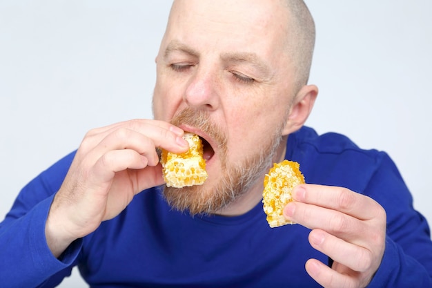 Bärtiger Mann in einem blauen Pullover, der eine Wabe isst