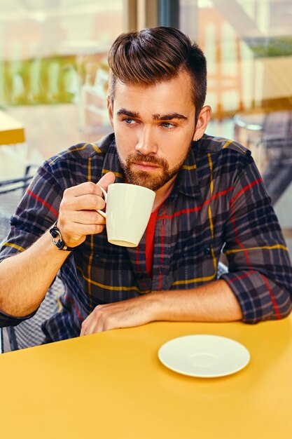 Foto bärtiger mann in einem fleecehemd, trinkt kaffee in einem café.