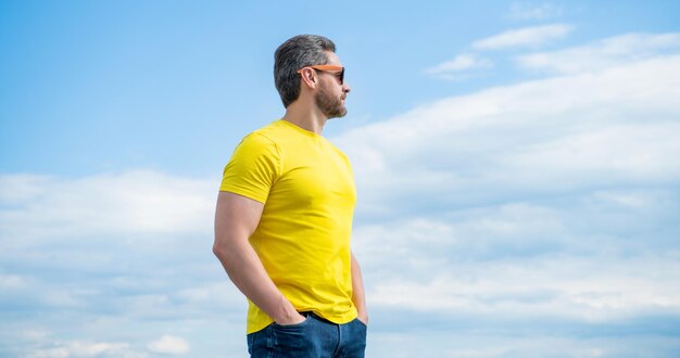 Bärtiger Mann in gelbem Hemd und Sonnenbrille im Freien vor Himmelshintergrund
