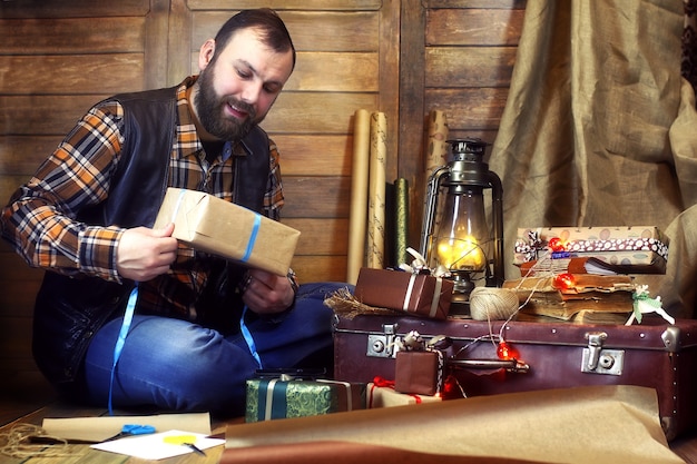 Bärtiger Mann in Hemd und Weste packt Weihnachtsgeschenke, die in einer Holzdekoration vor der Kamera posieren