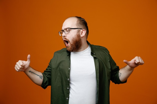 Foto bärtiger mann in lässiger kleidung mit brille, der glücklich und aufgeregt daumen nach oben zeigt, die über orangefarbenem hintergrund stehen