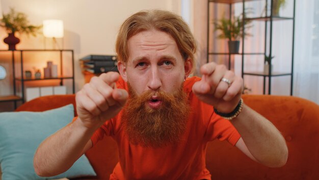 Bärtiger Mann lächelt und zeigt auf die Kamera, wählt den glücklichen Gewinner aus, und lädt zu Hause ein.