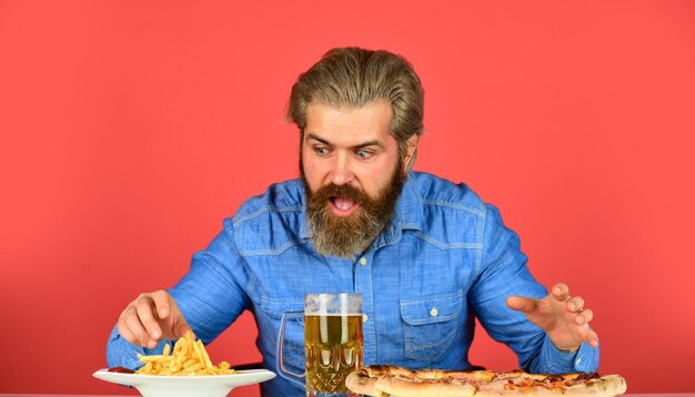 Bärtiger mann mit bier und pizza italienisches essen pommes-frites-typ in der bar trinkt bierglas und isst pizza prost beim fußballgucken im fernsehen amerikanisches fast food Premium-Foto
