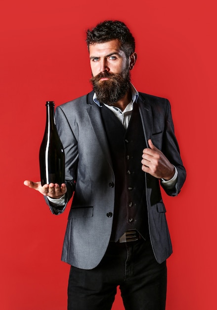 Bärtiger Mann mit einer Flasche Champagner und Glas. Stilvoller Mann im Smoking, Anzug, Jacke. Mann, der Flasche mit Champagner, Wein hält. Die Person hält eine Rotweinflasche in der Hand.