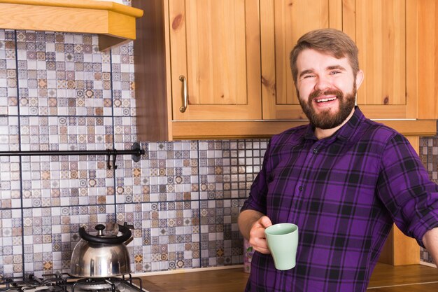 Bärtiger Mann mit Kessel, der Tee zum Frühstück zu Hause Küche macht
