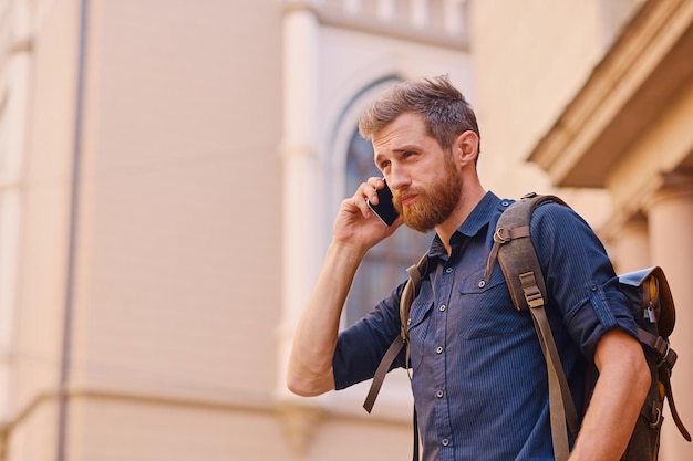 Bärtiger Mann mit Rucksack, der per Smartphone in einer alten europäischen Stadt spricht.