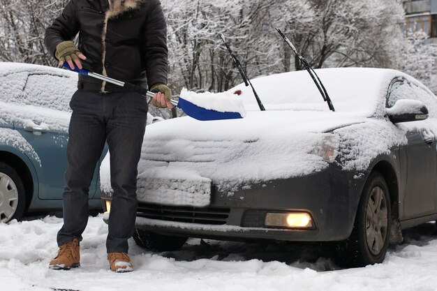 Bärtiger Mann reinigt an einem Wintermorgen Schnee von einem Auto