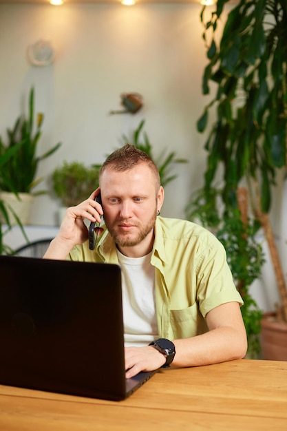 Bärtiger Mann spricht am Telefon mit Laptop