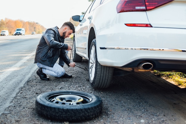 Bärtiger Mann wechselt Reifen seines Autos