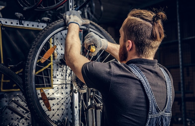 Bärtiger mechaniker repariert fahrradreifen in einer werkstatt. rückansicht, serviceanleitung.