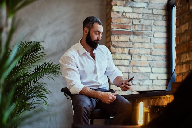 Bärtiger moderner Mann mit Smartphone in einem Raum mit Loft-Interieur.