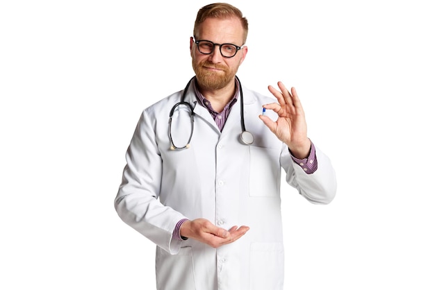Bärtiger reifer Mann mit Brille, Laborkittel und Stethoskop, Arzt hält isolierte Pillen und Medikamente in der Hand