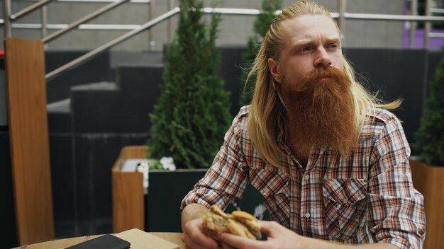 Bärtiger Student, der Burger im Straßencafé im Freien isst