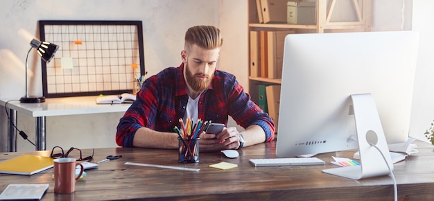 Bärtiger, stylischer Typ, der im Büro eine Nachricht am Telefon schreibt