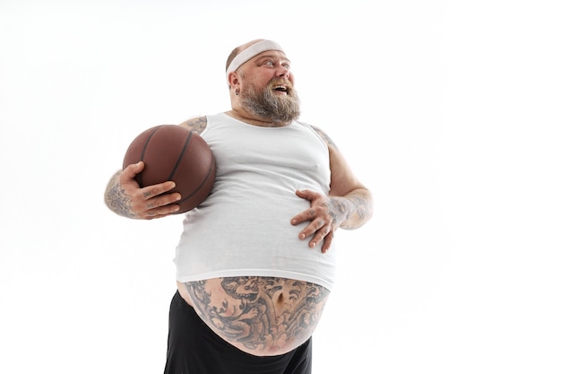 Bärtiger übergewichtiger tätowierter Mann mit Basketballball im weißen Hintergrund